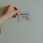A hand holding a motivational note with uplifting text in an indoor setting.
